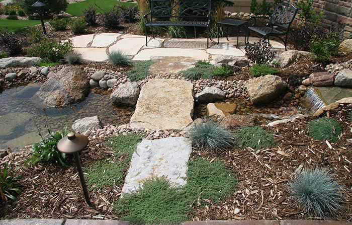 A natural stone bridge leads to a waterside patio.
