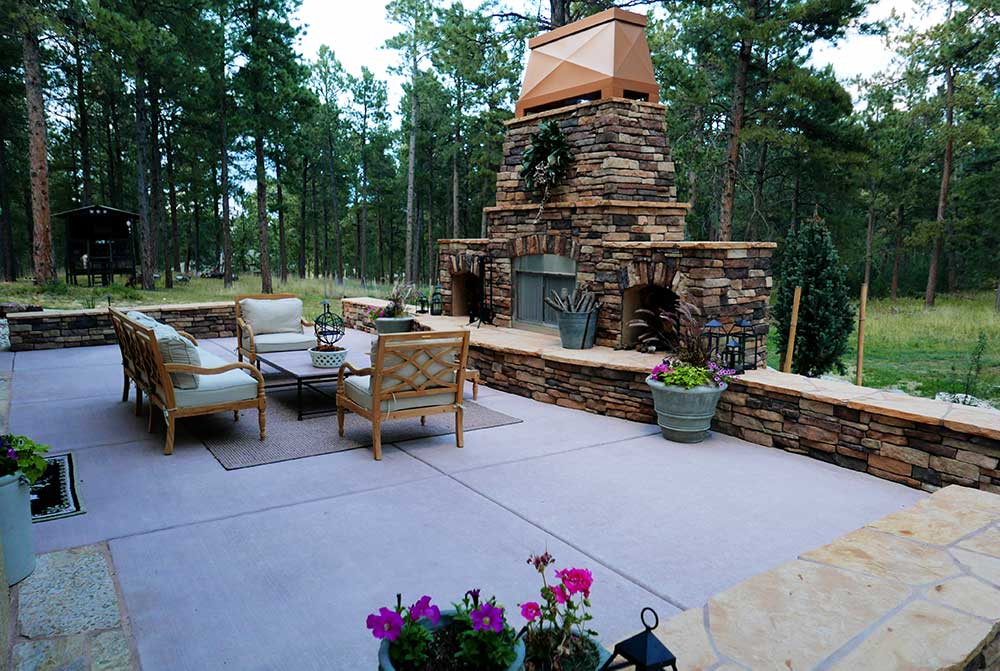 Outdoor patio with fireplace, container plants, dining area, and stone sitting wall.