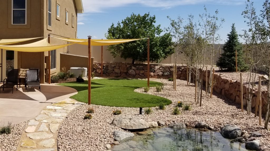 Artificial turf backyard with rock garden, awning, and pond 
